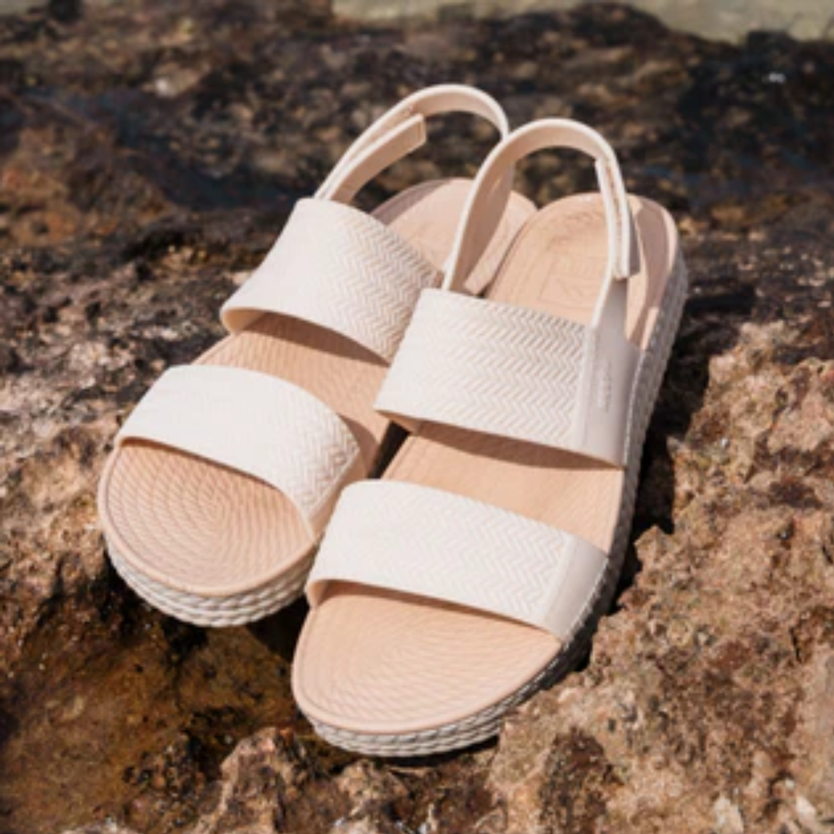 The REEF Water Vista in Vintage Oasis by REEF, a pair of beige sandals with espadrille braids and woven textures, rests on rocks under the sun. Made from water-friendly materials, they offer style and durability for sunny adventures. Main image