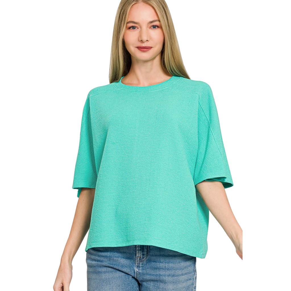 A woman wears the Zenana Double Knit Short Sleeve Top in turquoise with blue jeans, standing against a white background.