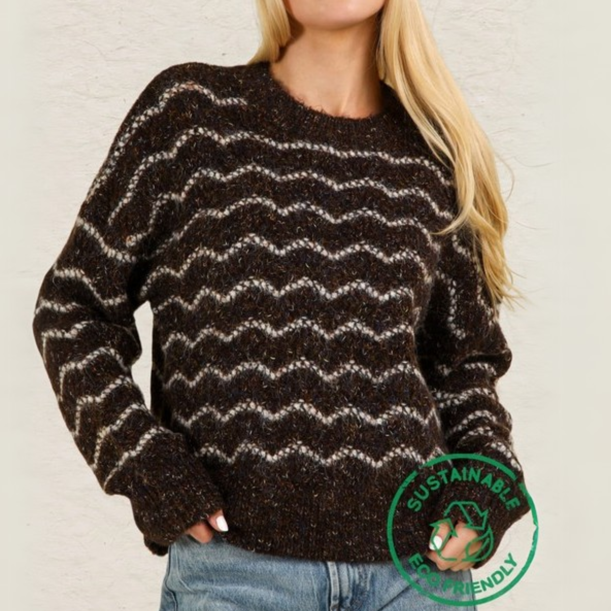 A person wearing Fashiongo's ECO Wave Striped Soft Knit Pullover Sweater Top with a brown and white zigzag pattern stands against a light background. A "Sustainable Eco-Friendly" badge emphasizes its commitment to slow fashion.