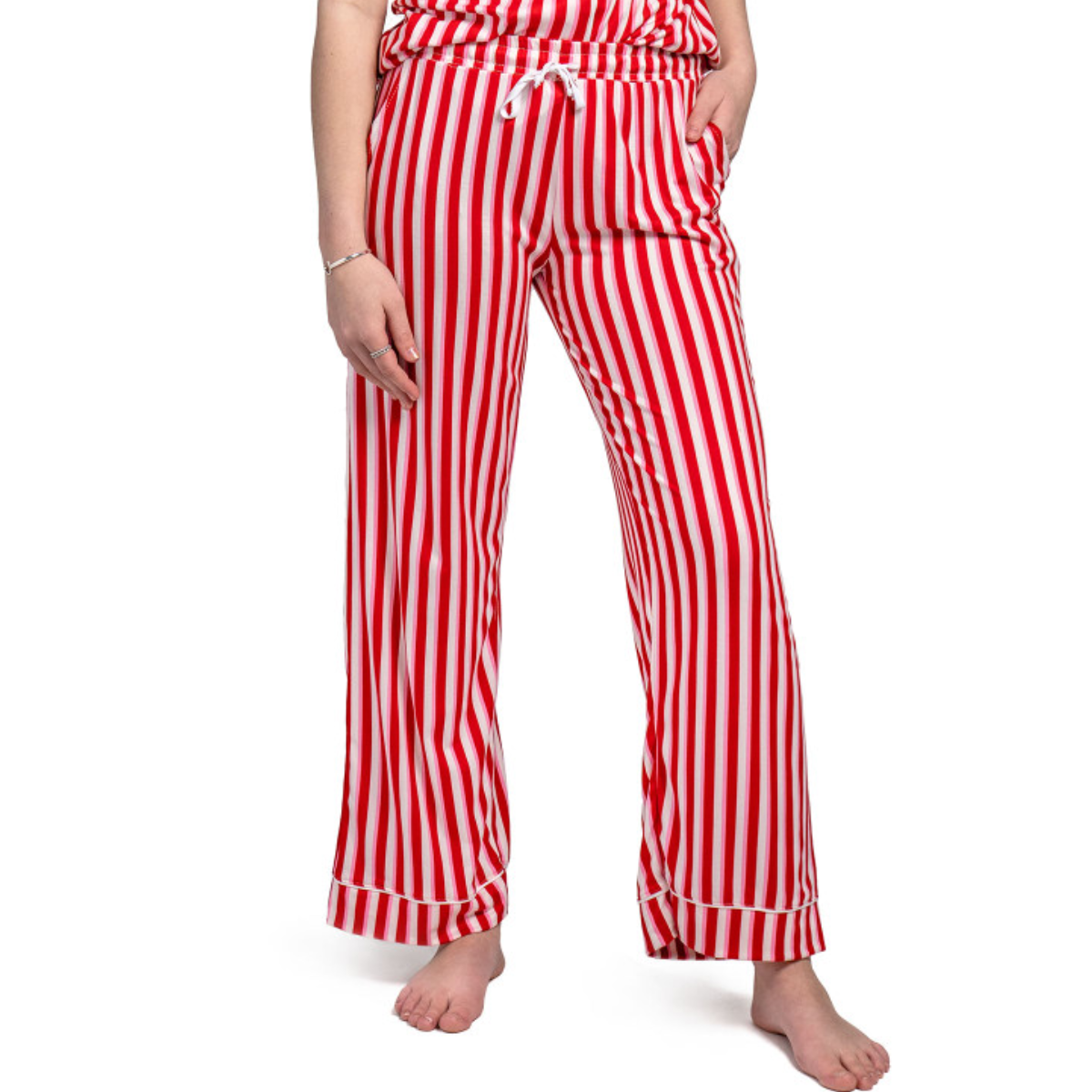 A person stands barefoot on a white background, wearing DM MERCH HELLO MELLO HOLIDAY PANTS L/XL from DM MERCHANDISING INC in red and white stripes, with hands in pockets. Designed to fit sizes 12-16 comfortably.