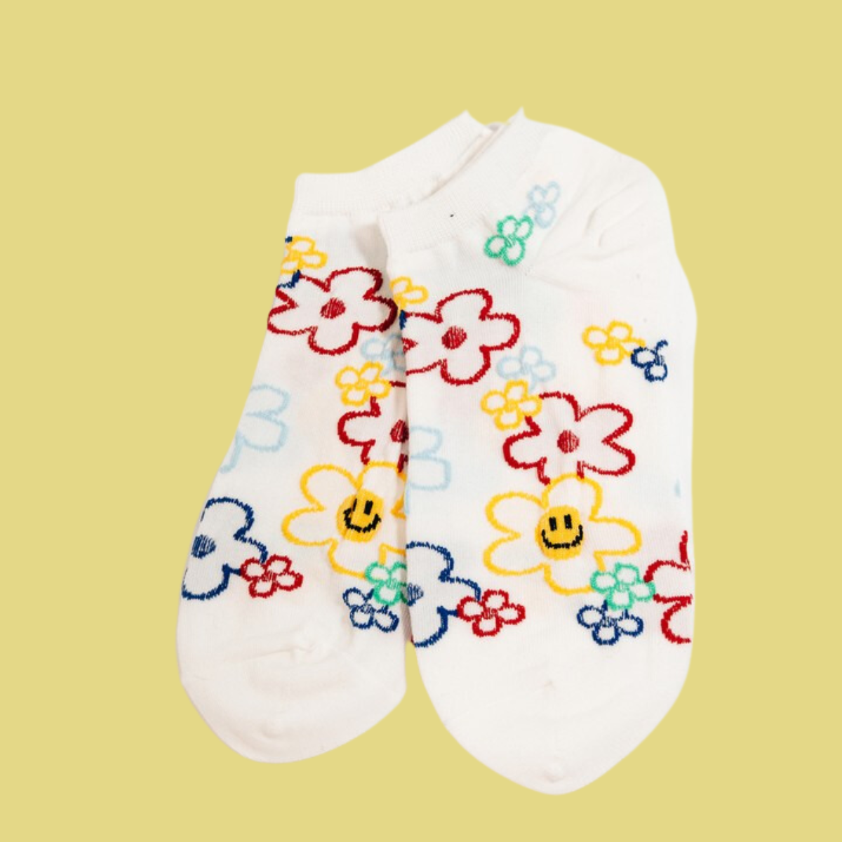 Smiley Socks by Flipflops & Whatnots feature a white base adorned with colorful floral patterns and smiley faces, set against a solid yellow background.