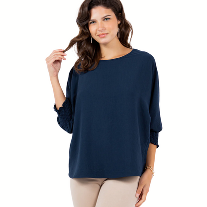 A woman wears the LTX Air Flow Top with smocking cuffs in navy blue and beige pants, standing against a white background.