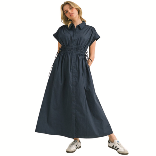 A woman wears the Jodifl Cotton Poplin Shirt Midi Dress With Pockets in navy blue, featuring a collared neck, short sleeves, and a wrinkle waistline, paired with white and gray sneakers against a white backdrop.