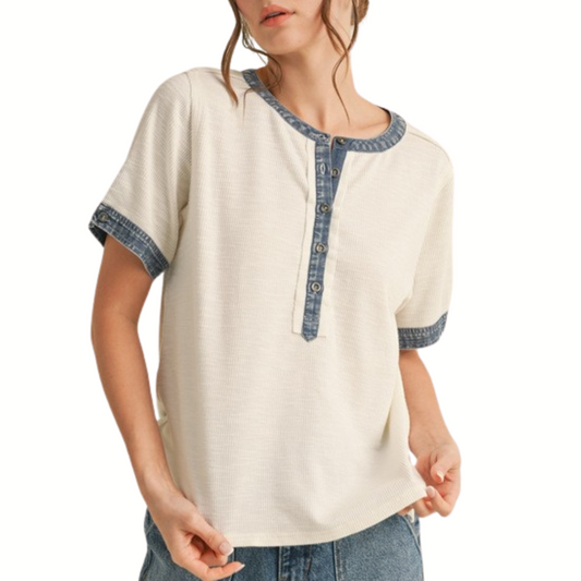 A woman wears the FASHION GO Ribbed Henley Neck Short Sleeves Top in cream, featuring blue denim trimming on the collar, placket, and cuffs, paired with blue jeans.