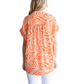 A woman with blonde hair, seen from behind, wears the FASHION GO Tiger Print Collared Button Up Top in orange and white with white pants against a plain white background.