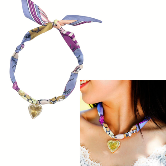 The FASHION GO Scarf Necklace Purple with Gold Rhinestone Heart features a knotted, multicolored design and a sparkling heart pendant. Shown on a white background and elegantly worn around a woman's neck.