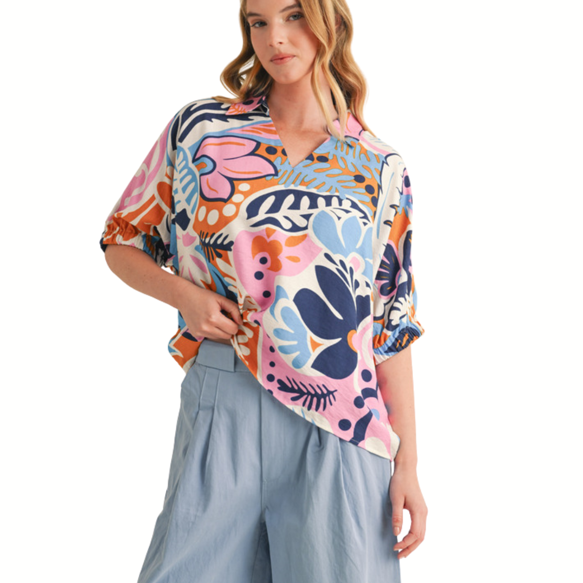 A woman stands against a white background wearing the FASHION GO Multicolor Print 1/2 Sleeves Top with an open collared neck and light blue high-waisted shorts.