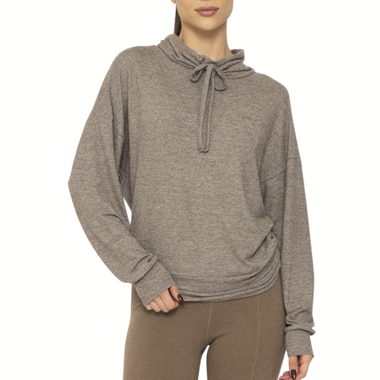 A person wears the Mono B Brushed Cowl Neck Lounge Pullover in Olive with a relaxed fit, paired with brown leggings, standing against a plain white background.