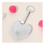 The Wona Trading Bling Heart Key Chain Bag Charm Assorted Colors features a silver heart with rhinestones, surrounded by three pink and one white pom-pom on a beige surface—making it a perfect sparkly accessory.