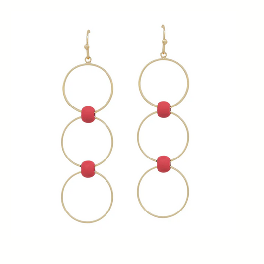 The Red and Gold Layered Circle Earrings by What's Hot feature three linked gold rings, each accented with a central red bead for a dainty look.
