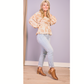 A woman poses indoors with one leg bent, wearing a patterned beige blouse, light blue jeans, and the Vanish Side Dip Ankle Boot in Taupe by CORKY'S FOOTWEAR INC, smiling against a light purple wall and wood floor.