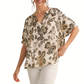 A woman wears the Fashiongo Flower Print Short Dolman Sleeves Top, a relaxed fit cream blouse with black and gold floral patterns, styled with light-colored pants.