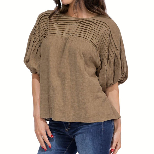 A woman wears the FASHION GO Puff Sleeve Blouse—a loose-fitting, brown top featuring chest pleats and puff sleeves—paired with blue jeans for effortless, chic style.