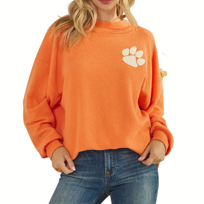 A woman wears the Tres Bien Paw Print TIGERS Cloudy Knit Top in orange with a varsity paw print graphic on the chest, paired with blue jeans.