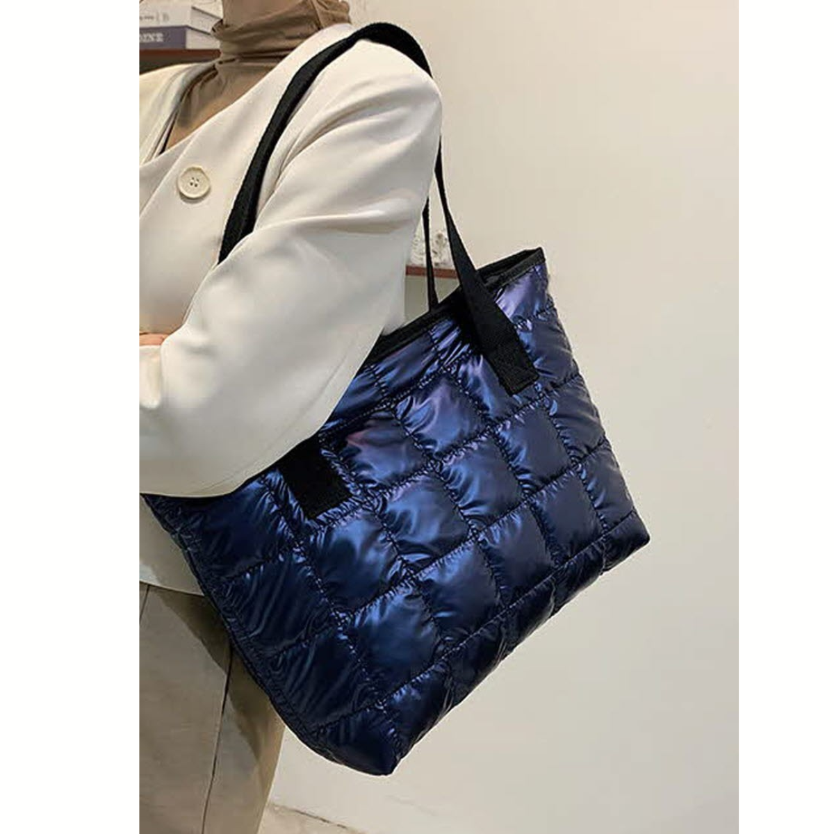A person carries the FASHION GO Quilted Shoulder Tote Bag - Assorted Colors, a large shiny puffer tote with black shoulder straps, while wearing a light-colored jacket.