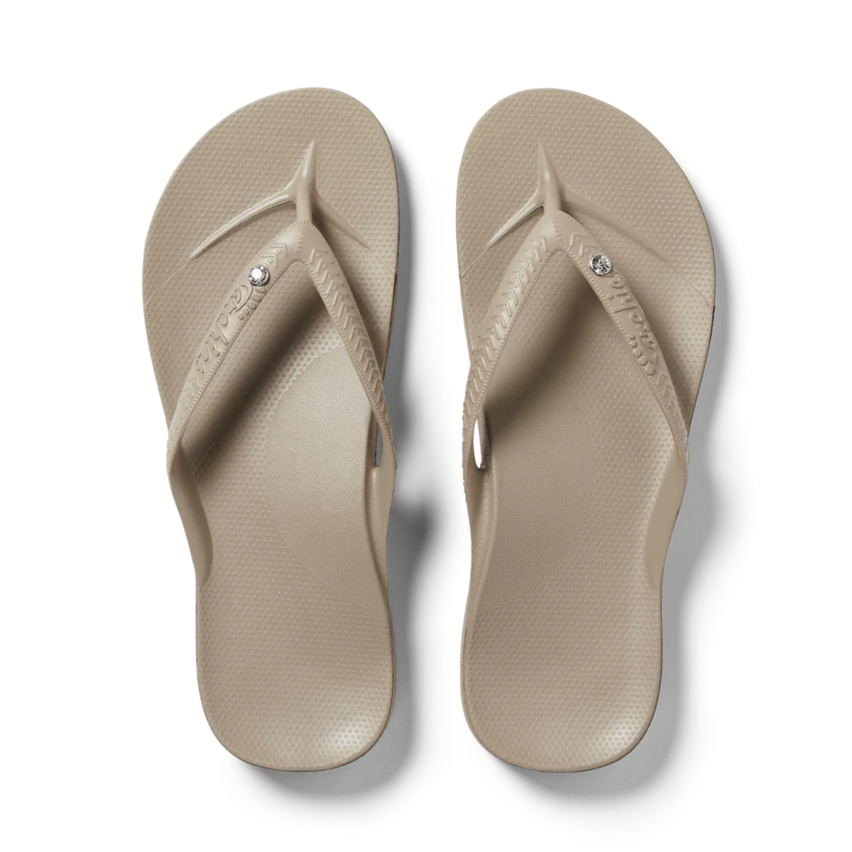 The Archies Arch Support Flip Flops Crystal in Taupe by ARCHIES FOOTWEAR LLC feature textured straps with a circular crystal detail, offering stylish comfort and support for those seeking fashionable arch-support sandals.