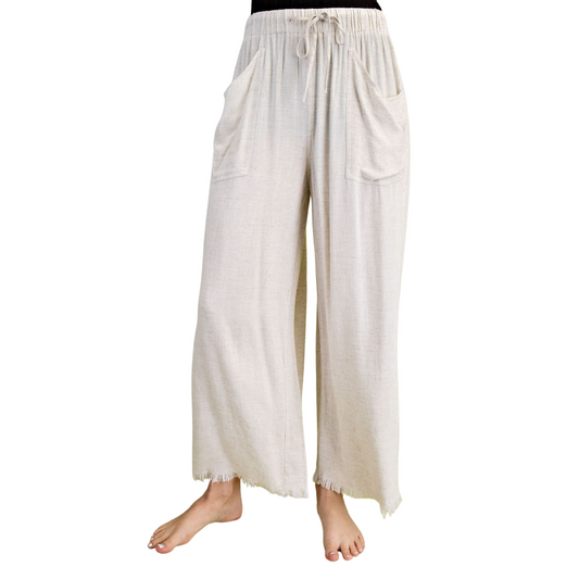 A person stands barefoot wearing FASHION GO Frayed Cropped Wide Leg Pants, made from a lightweight linen blend with a drawstring waist and pockets.