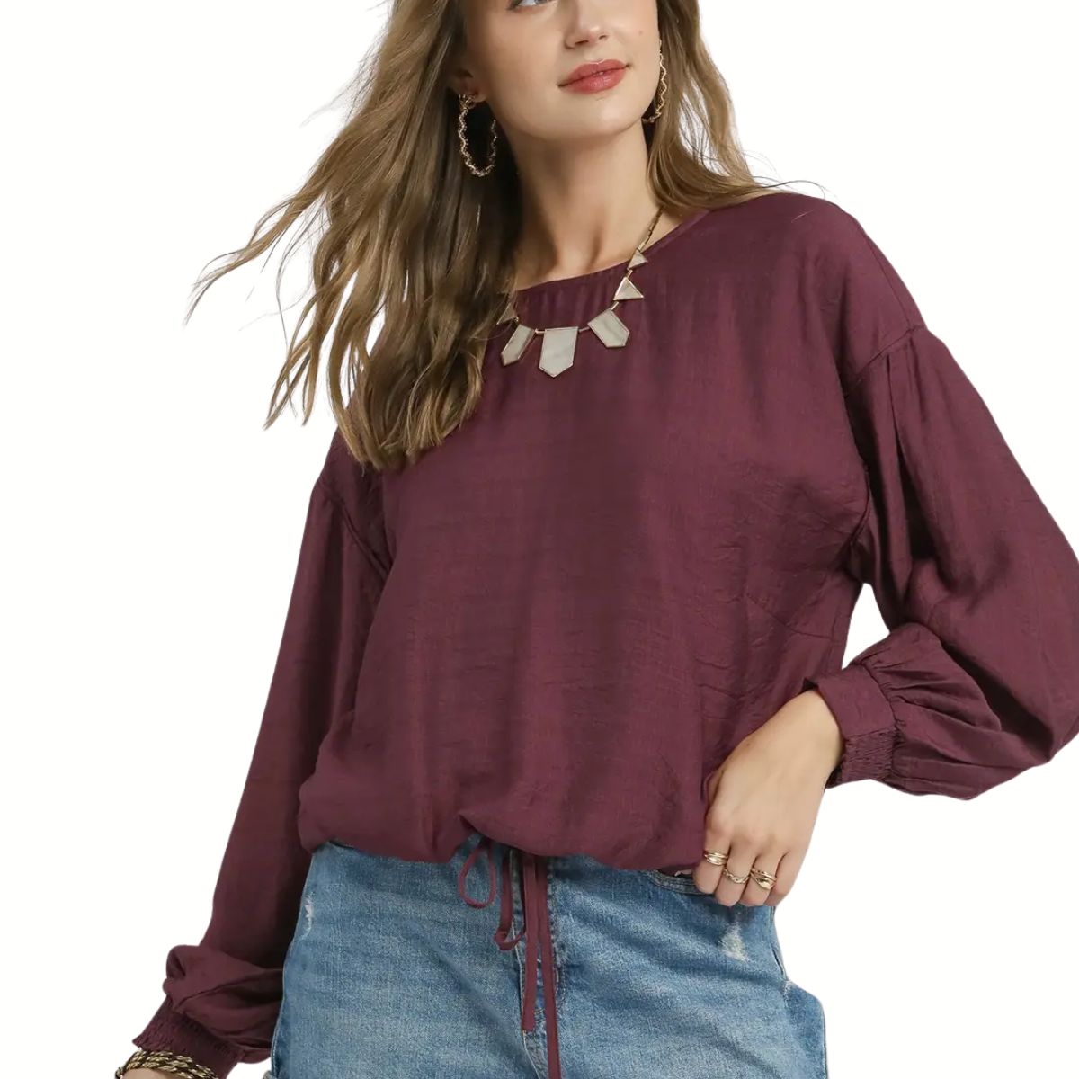 A woman models the Umgee Round Neck Long Sleeve Drawstring Blouse in maroon, styled with a denim skirt, statement necklace, and hoop earrings against a white background.