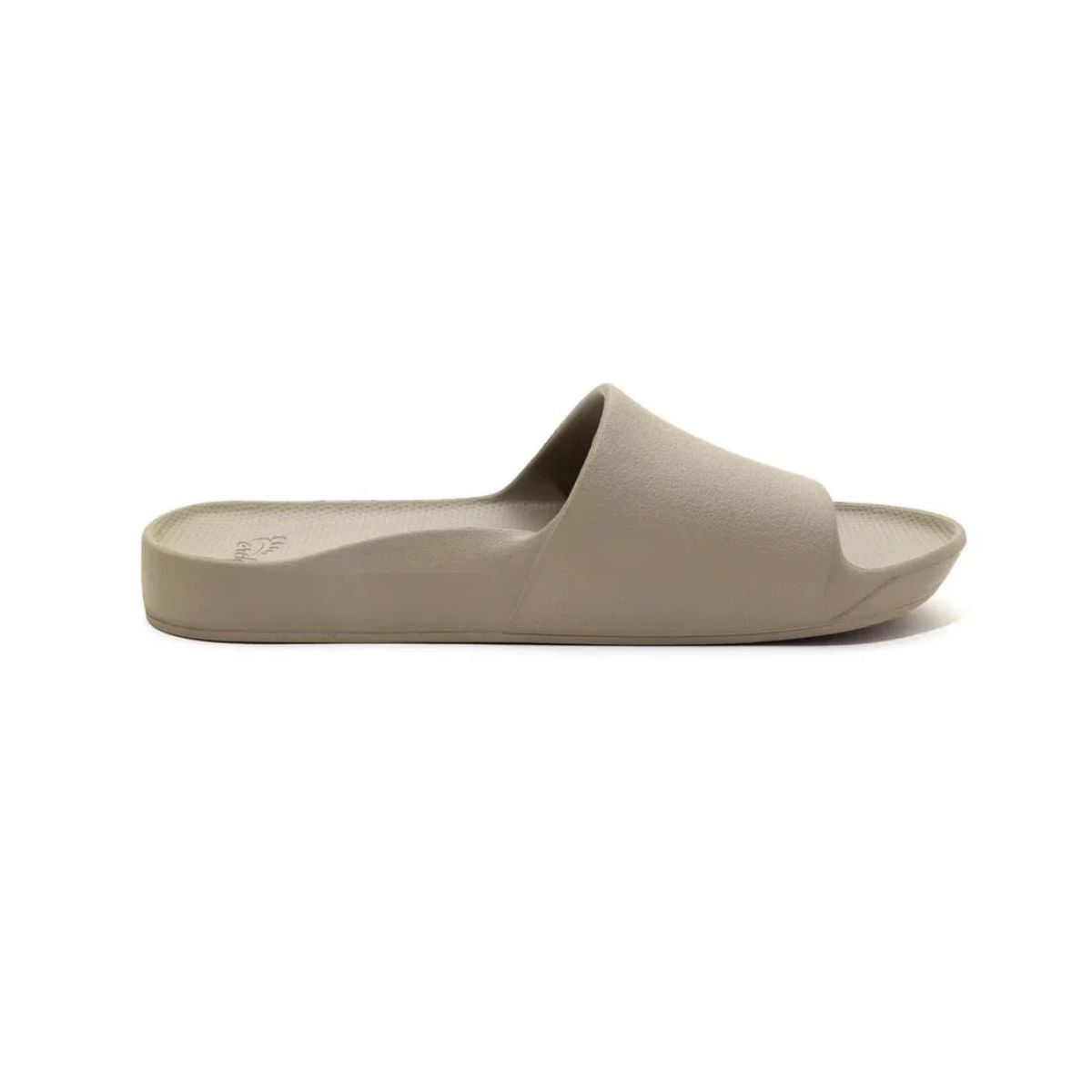 The Archies Slide Sandal in Taupe by ARCHIES FOOTWEAR LLC features a wide strap and contoured footbed. Displayed from the side on a white background, these beige slip-on slides offer excellent support.