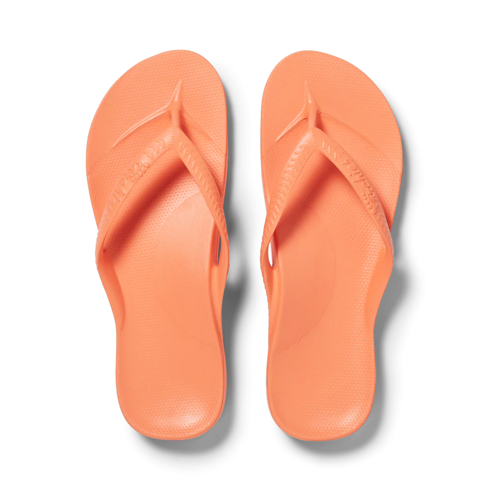 A pair of ARCHIES FOOTWEAR LLC Archies flip flops in Peach arranged neatly against a black background.