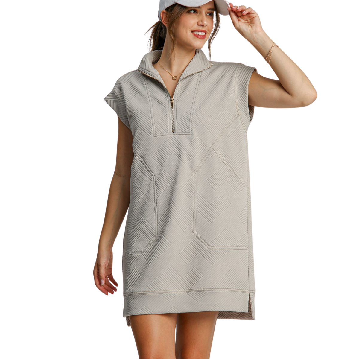 A woman wearing a cute, light gray, poly spandex blend Zip Front Knit Sporty Dress by FASHION GO smiles while adjusting her baseball cap.