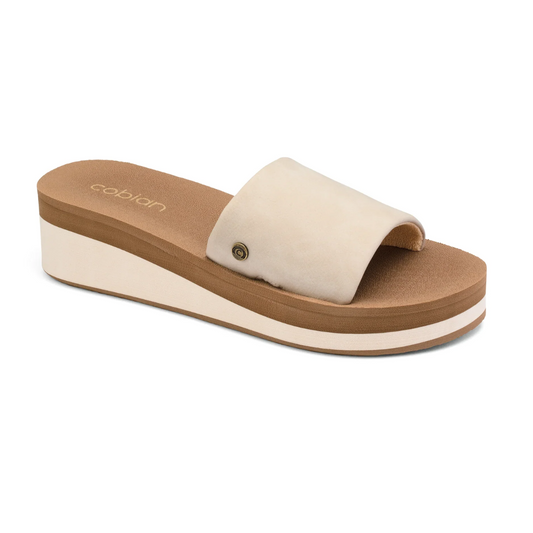 The Seville Wedge Slide in Taupe by COBIAN boasts a thick sole and a wide, single upper strap. The cushioned top sole provides anatomical arch support and is adorned with the Cobian logo on the insole.