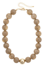 The Marjorie Fall Beaded Necklace by Canvas Style features chunky, brown marbled resin beads accented with a statement gold bead at the center and is finished with an adjustable gold chain clasp.