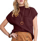 A woman wears a burgundy top and brown buttoned skirt, accessorized with a wooden necklace and bracelet, ideally paired with Shewin's Patch Pocket Ribbed Knit Short Sleeve Sweater for modern casual style in transitional weather.