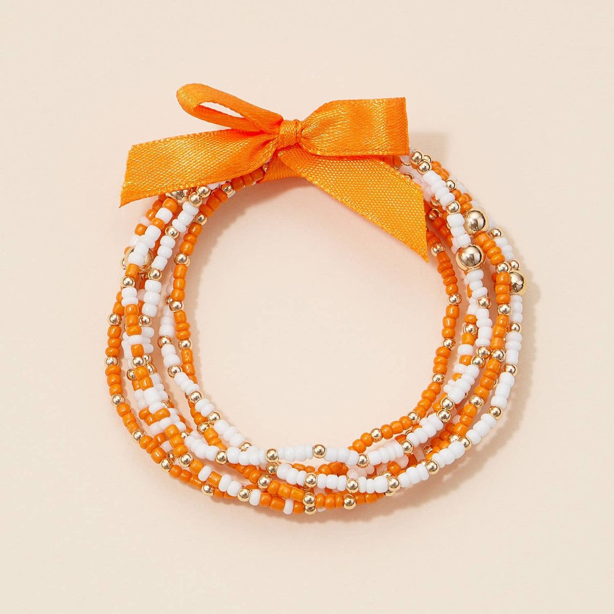 A Game Day Seed Beaded Bracelet Set consisting of four colorful seed beaded bracelets in orange, white, and metallic gold, tied together with an orange ribbon bow.