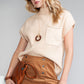 A woman in sunglasses wears a Shewin Patch Pocket Ribbed Knit Short Sleeve Sweater in light beige, paired with a brown skirt and clutch. Her long blond hair cascades over a necklace with circular pendants, creating perfect vibes for transitional weather.