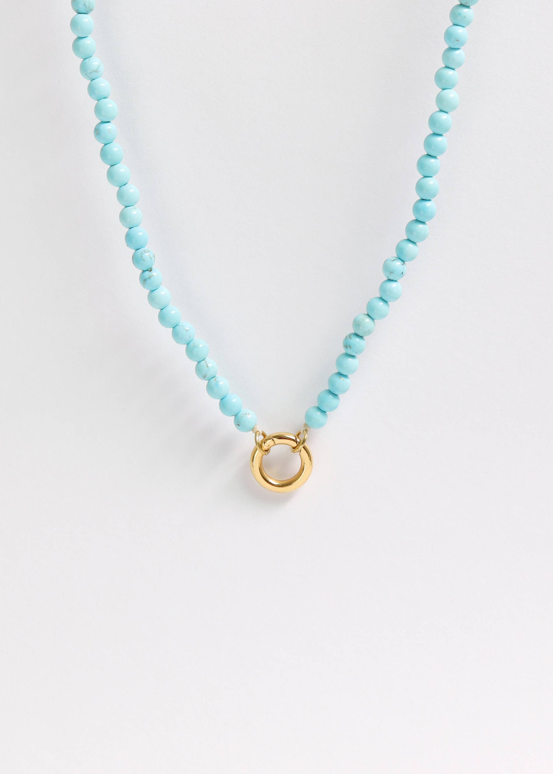 A close-up of the WJW Semi Precious Natural Stone Charm Keeper Necklace, featuring round turquoise beads and a central 18K Gold PVD Coated circular clasp, displayed on a plain white background.