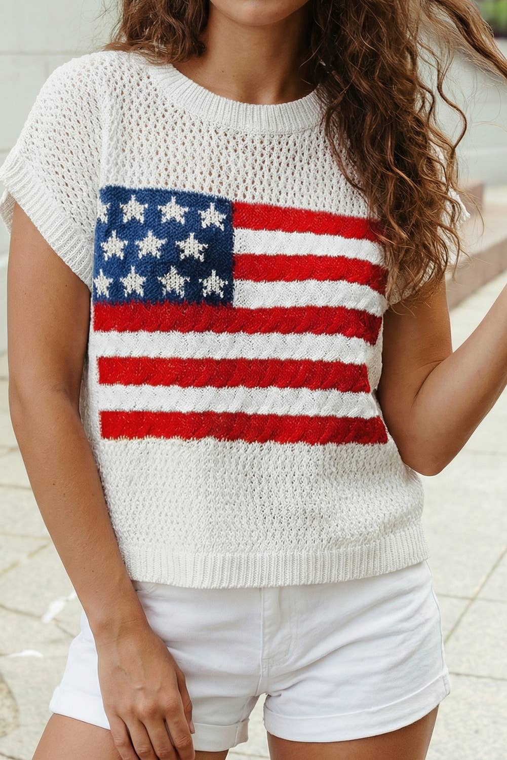 A woman outdoors wears the 1 the Woman Flag Graphic Short Sleeve Sweater Top paired with white shorts, showcasing an American flag design.