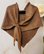 The JC Sunny Fashion Cashmere-Blend Knit Triangle Shawl with Cross-Front Design, in brown, is tied loosely and displayed against a light background with a white artificial rose partially visible on the right.