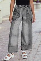 A person in a black top, 1 the Woman Drawstring Seam Detail Raw Hem Wide Leg Denim Pants, and white platform sandals stands on a paved sidewalk.