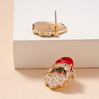 The Pearl Santa Claus Stud Earrings from Lilla Haven feature gold-tone holiday charm with pearl accents, displayed on a flat surface with the earring back and pin visible beside it and partially resting on a white block—these festive Christmas Holiday Earrings make a delightful gift for the season.