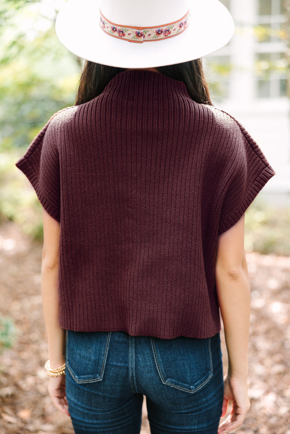 A person with casual style stands outdoors, embracing the transitional weather, wearing a wide-brimmed hat and Shewin's Patch Pocket Ribbed Knit Short Sleeve Sweater resembling a cozy poncho.