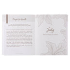 The One-Minute Devotions for Women Softcover by Christian Art Gifts is open to a page titled “July: When things go wrong,” featuring a prayer for growth, reflections on learning from children, and elegant flower line art. The pages provide uplifting one-minute devotionals designed especially for women.