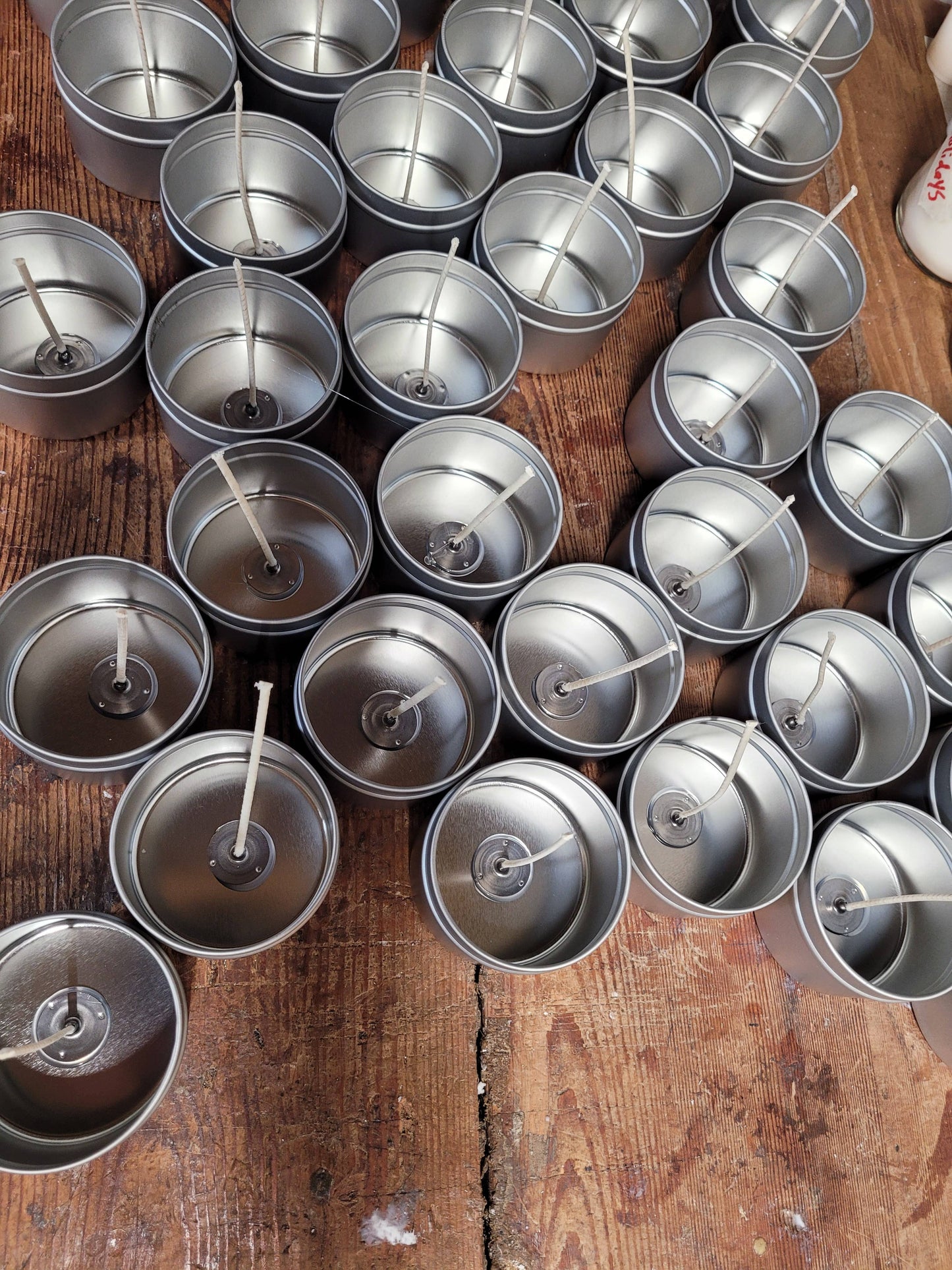 On a wooden surface, several 4oz tin containers are prepared with wicks, including wood wicks, for making Stephanie Henry Candle Company's Mahogany Teakwood hand-poured soy wax candles.