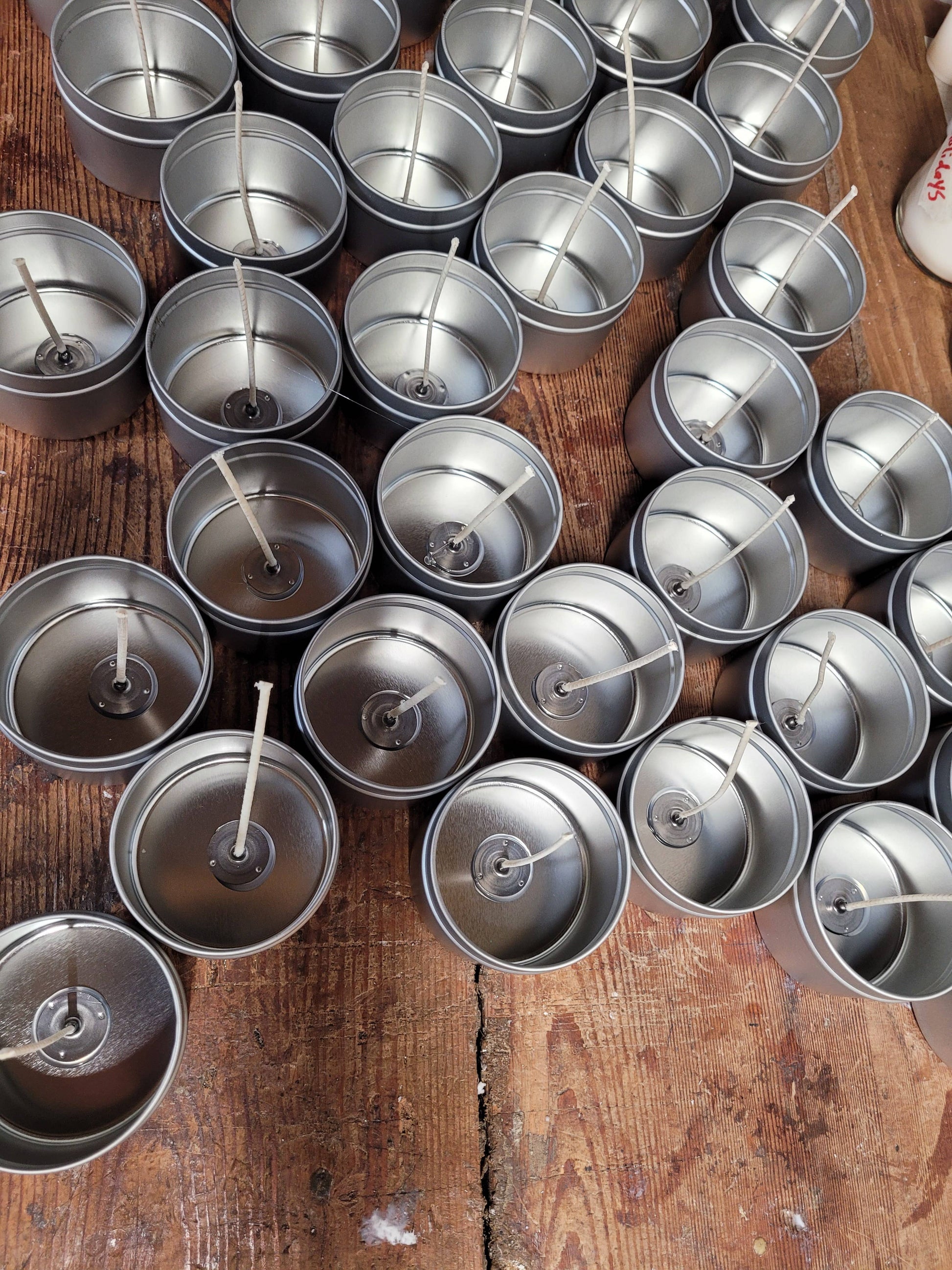 Multiple 4oz tins from Stephanie Henry Candle Company, complete with wicks, are arranged on a wooden surface, ready to become hand-poured soy wax candles featuring the scent "Under the Cabana.