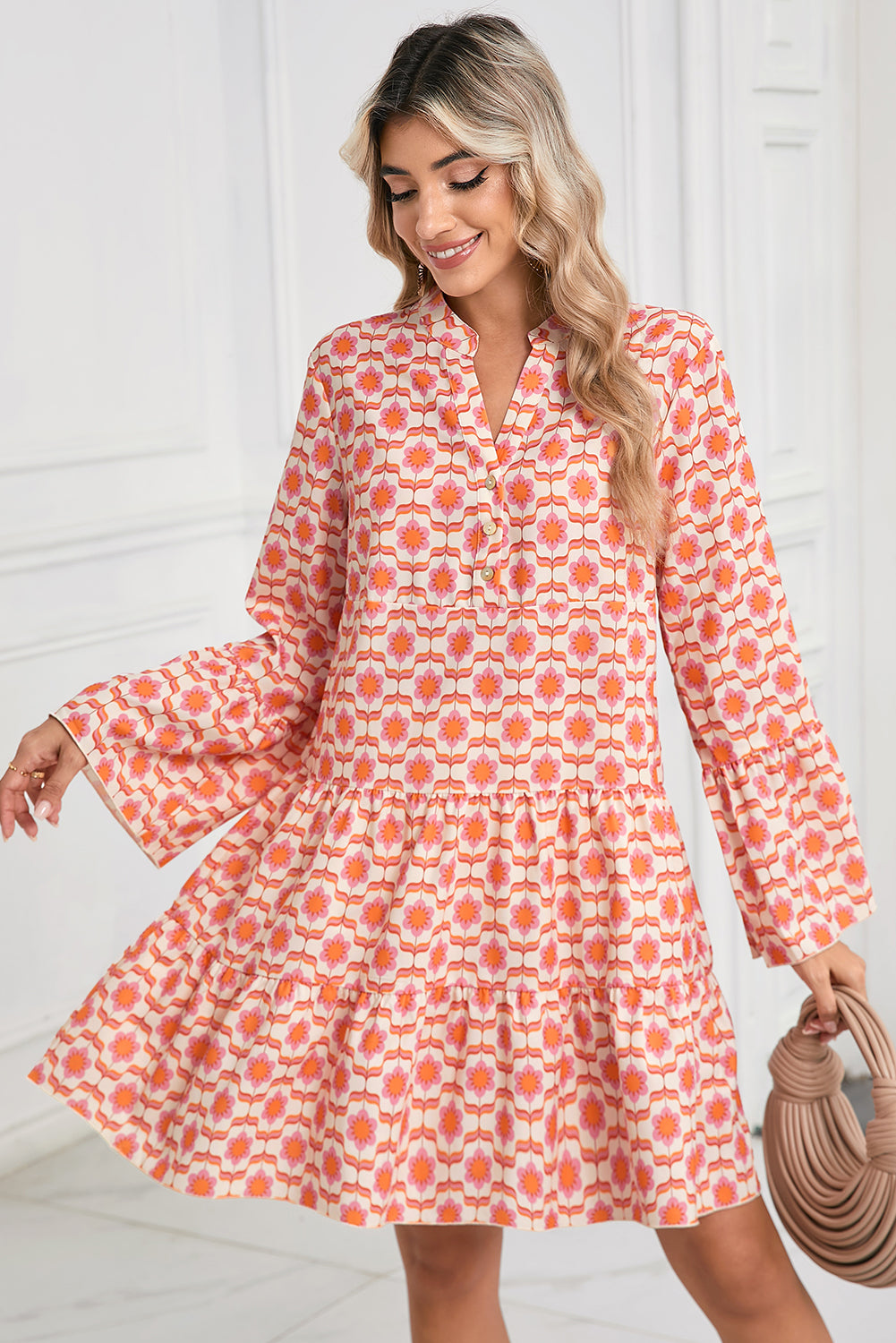 A person wearing a Shewin Orange Floral Button V Neck Bell Sleeve Mini Dress is smiling and holding a small, textured purse.