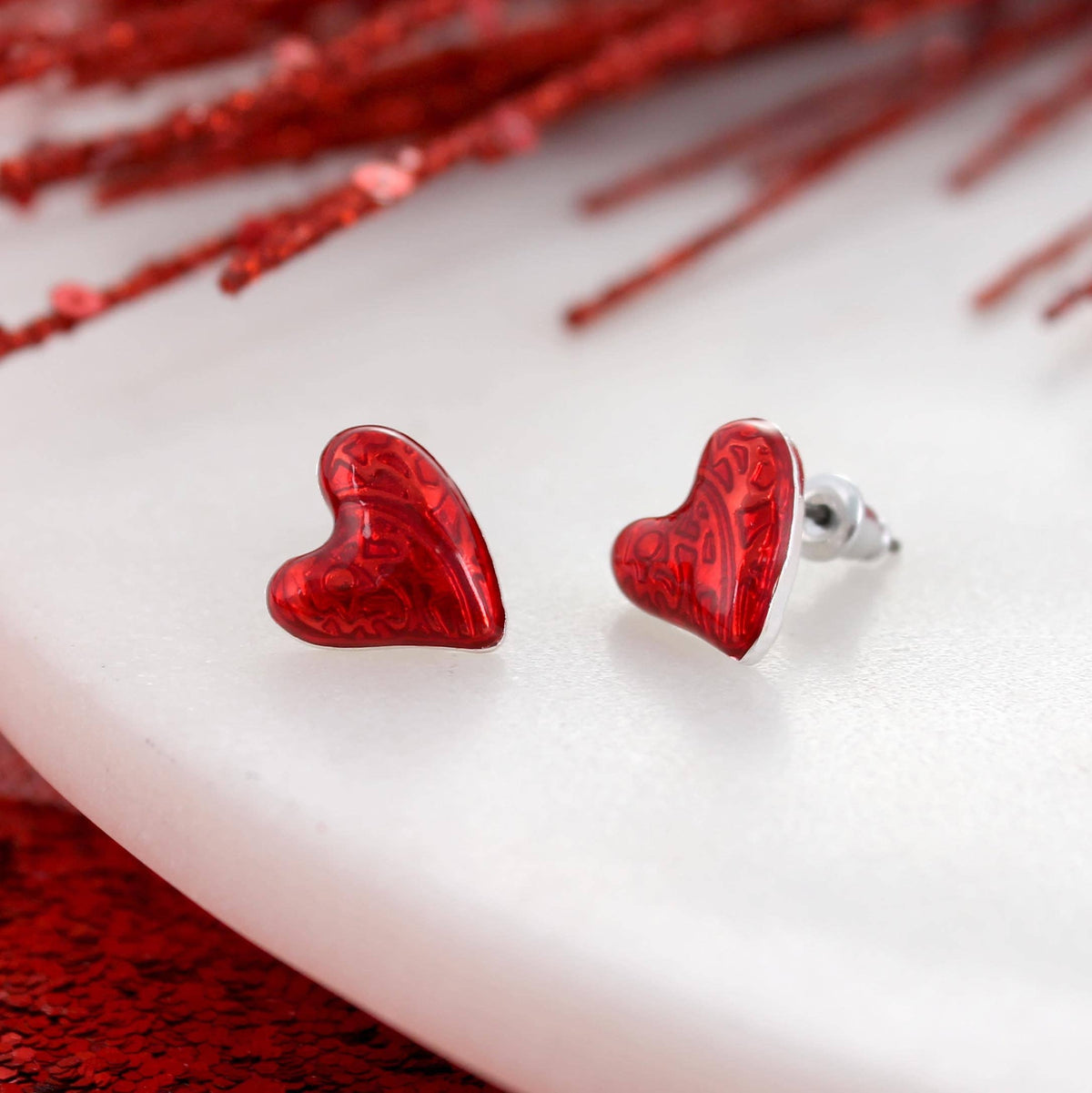 Add a touch of romance to your look with the Puffy Heart Valentine’s Day Stud Earrings by Seasons Jewelry—red puffy heart earrings featuring a subtle pattern, beautifully displayed on a white surface with red accents in the background, making them the ideal Valentine’s Day jewelry.
