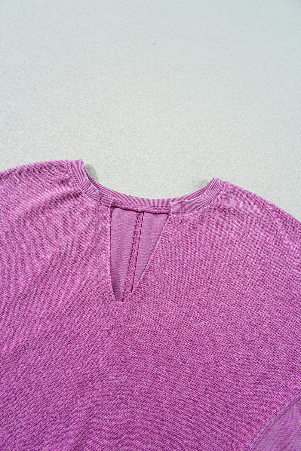 A pink Shewin sweatshirt with a notched neck and exposed seams is spread flat on a light background, showcasing its high-quality fabric.