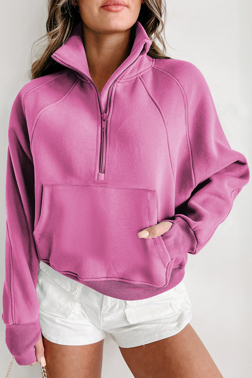 A person wears a gray, zip-up stand collar sweatshirt with ribbed thumbhole sleeves from Shewin, paired with white shorts.