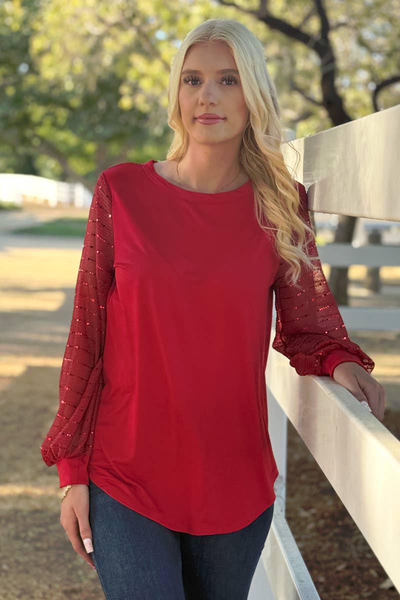 A woman with long blonde hair wears the 24-Hrs Fashion Sequin Sleeve Blouse and blue jeans while standing by a white wooden fence outdoors.