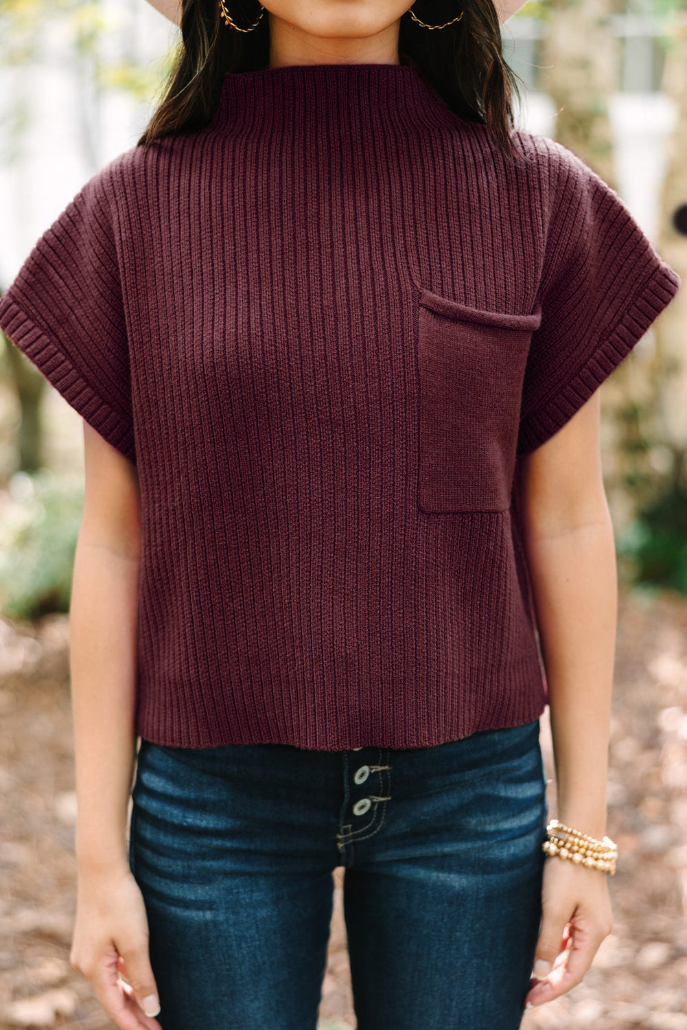 A person is outdoors wearing the Shewin Patch Pocket Ribbed Knit Short Sleeve Sweater, paired with dark jeans and gold bracelets.