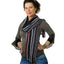 A person wearing a Boho Multi Stripe Oblong Scarf, which is a long, black-based scarf with thin, multi-colored vertical stripes and fringed ends.