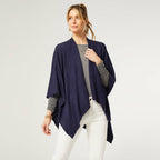 A woman faces slightly left against a light background, wearing the COCO + CARMEN Kiara Lightweight Wrap in navy blue over a gray top and white pants.