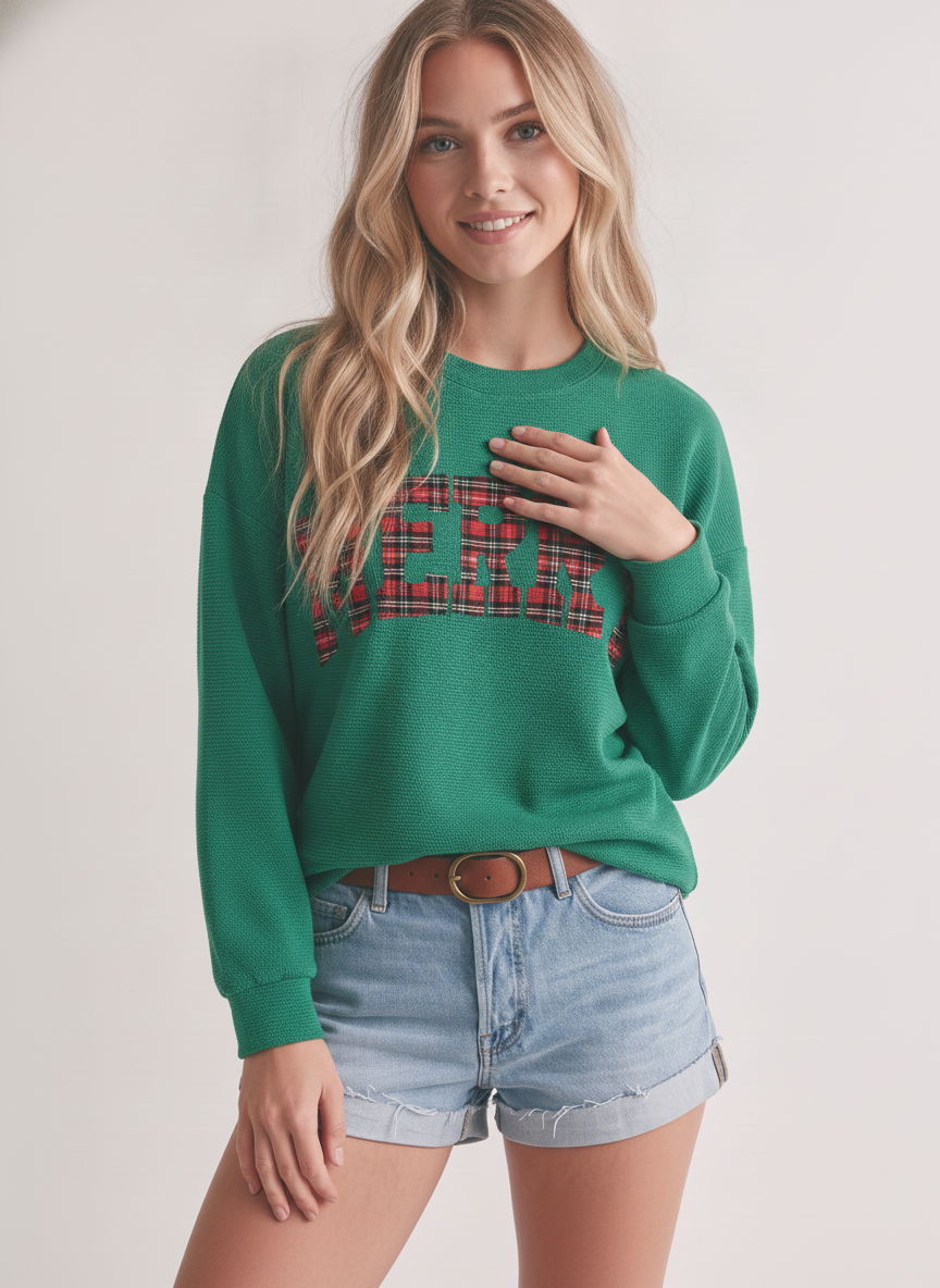 A person wearing a green Merry Plaid Cloudy Knit Top with light-wash denim shorts and a brown belt.