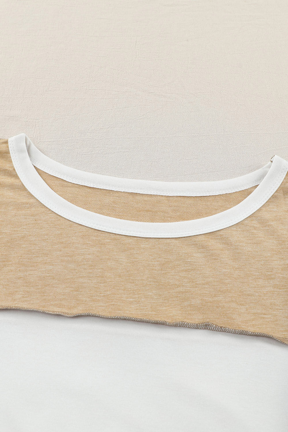 Close-up of the Shewin Khaki Color Block Exposed Seam Long Sleeve Top laid flat, focusing on the neckline and fabric texture, showcasing its versatile beige and white tones.