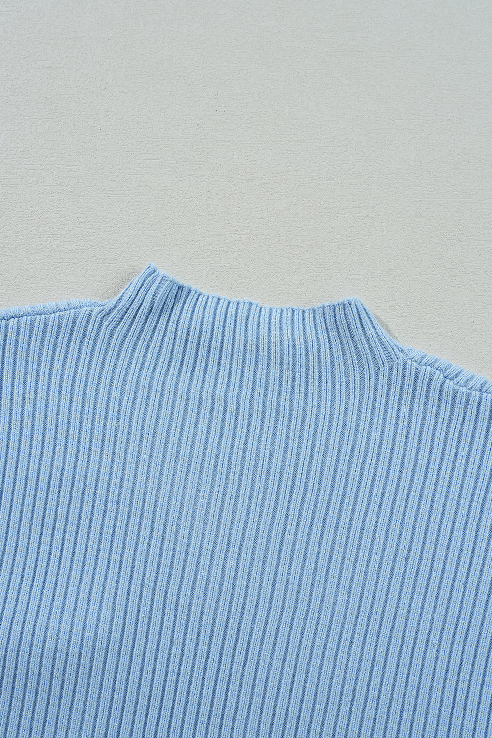 Close-up of Shewin's Patch Pocket Ribbed Knit Short Sleeve Sweater in light blue, featuring a high neckline, perfect for transitional weather, set against a beige background.